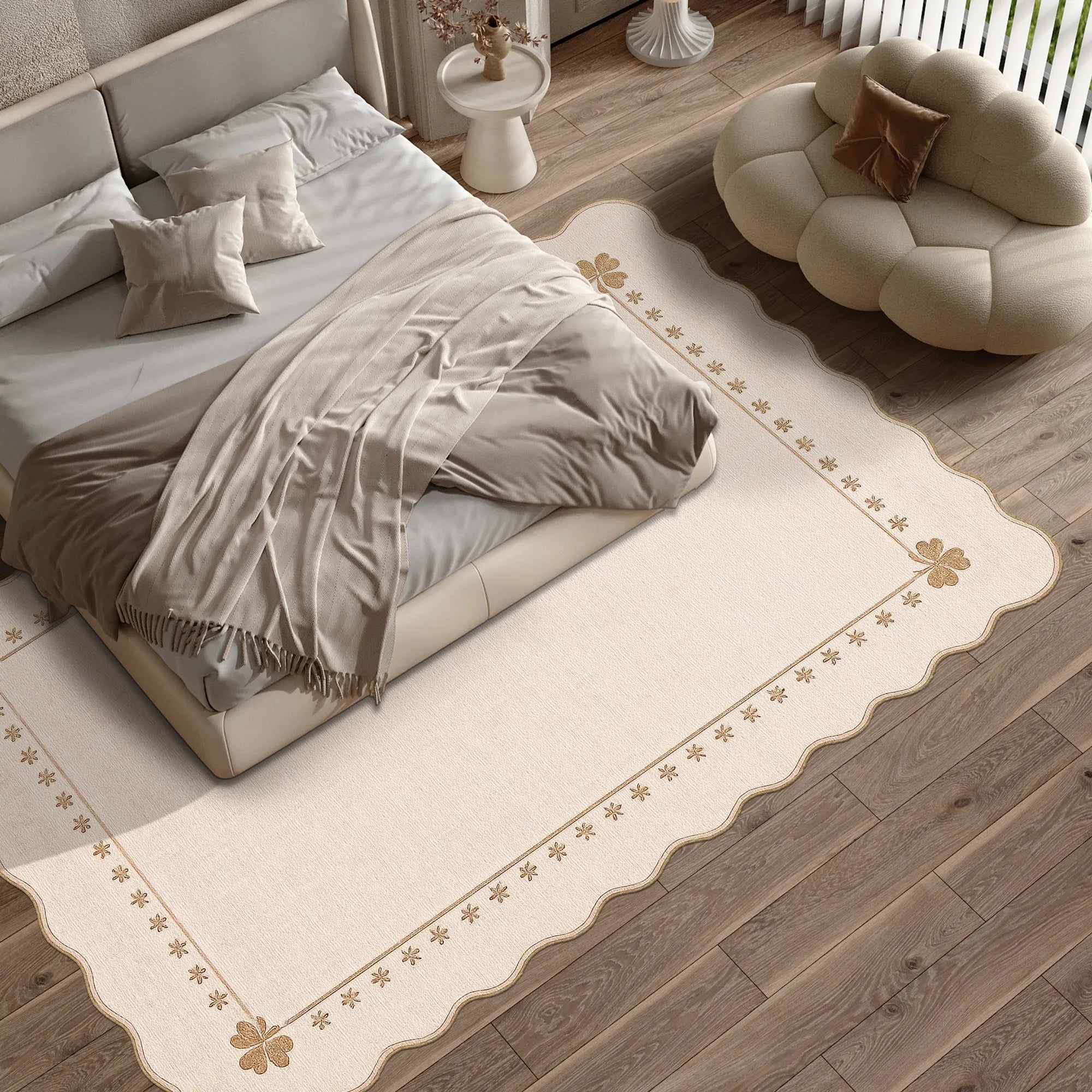 A cream-colored area rug with a scalloped border and gold floral motifs, styled in a modern bedroom setting under a bed with neutral-toned bedding.