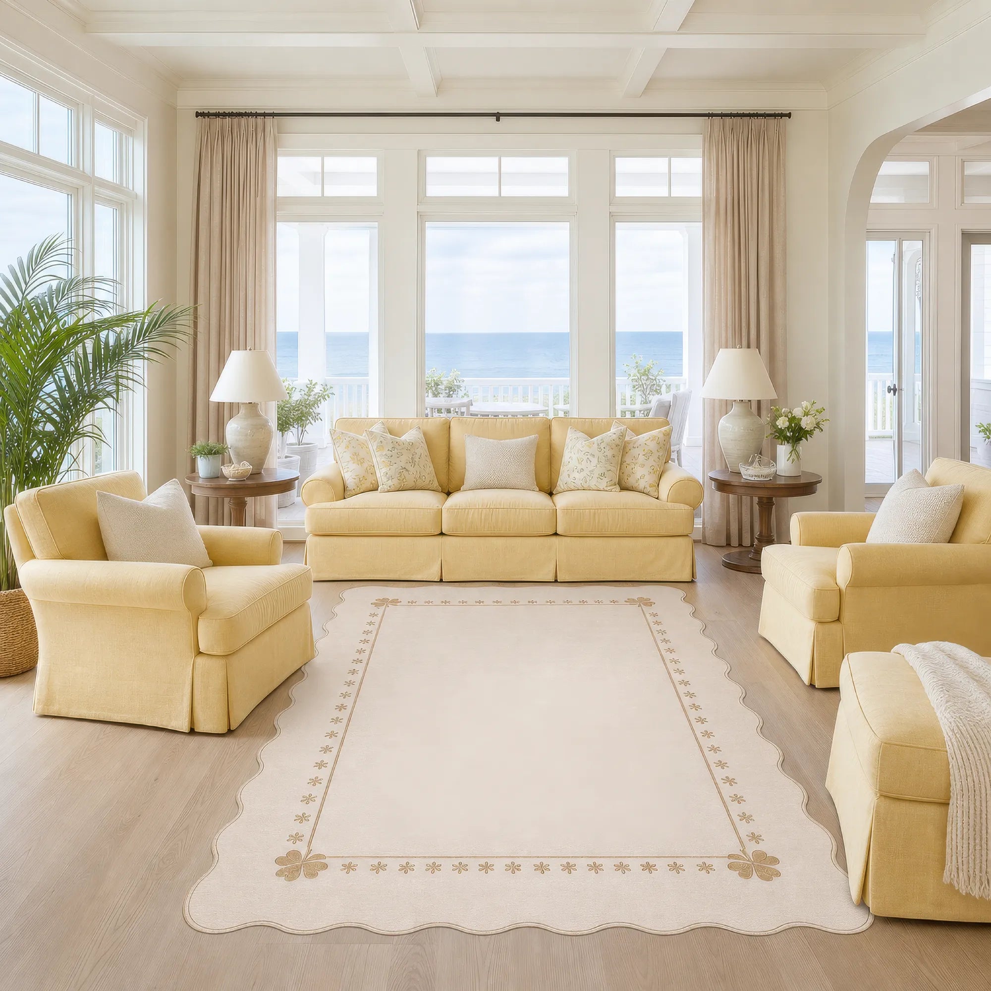 A cream scalloped area rug with scalloped edges and decorative border with a bright, modern living room featuring a pale yellow upholstered sofa, two matching armchairs, and large windows overlooking the ocean.