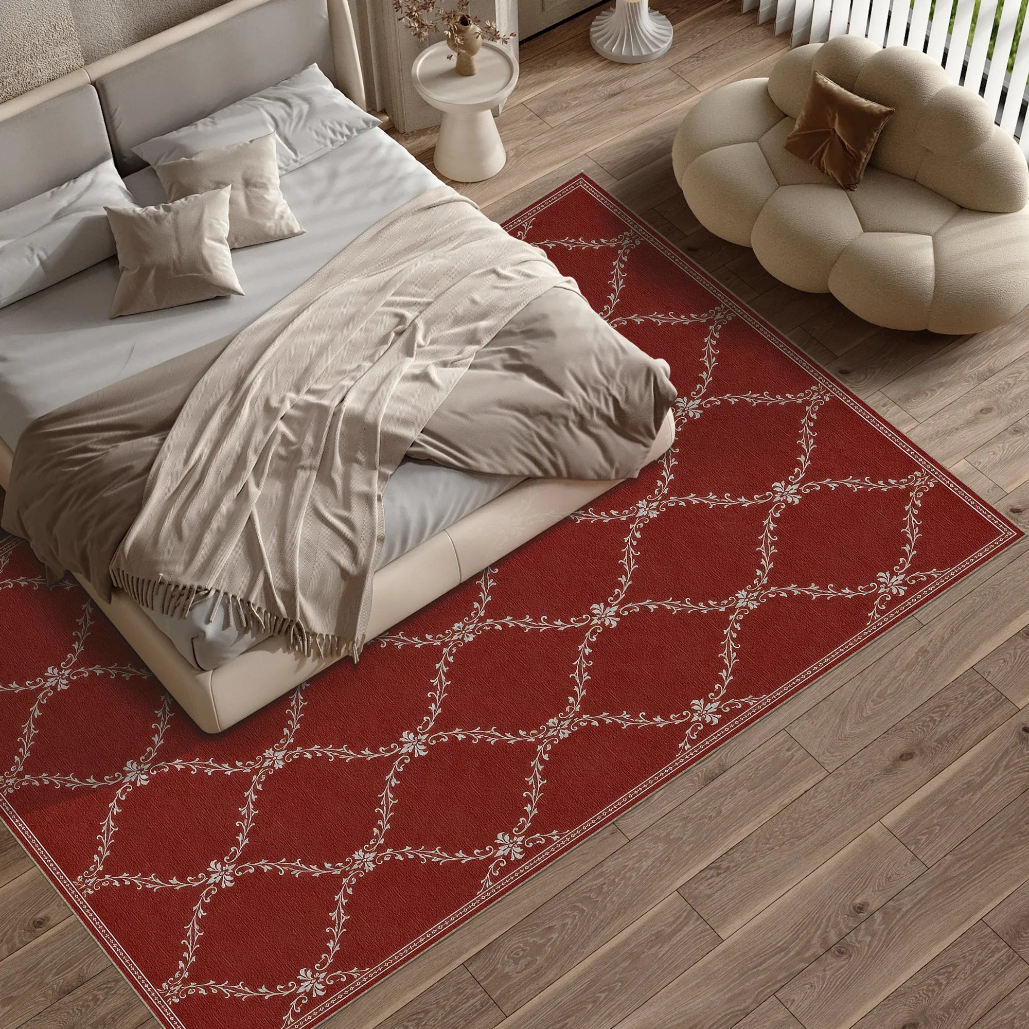 A red lattice area rug with a white geometric lattice pattern is styled on a light wood floor in a modern bedroom setting, surrounding a bed with beige linens and a cream cloud-shaped pouf.