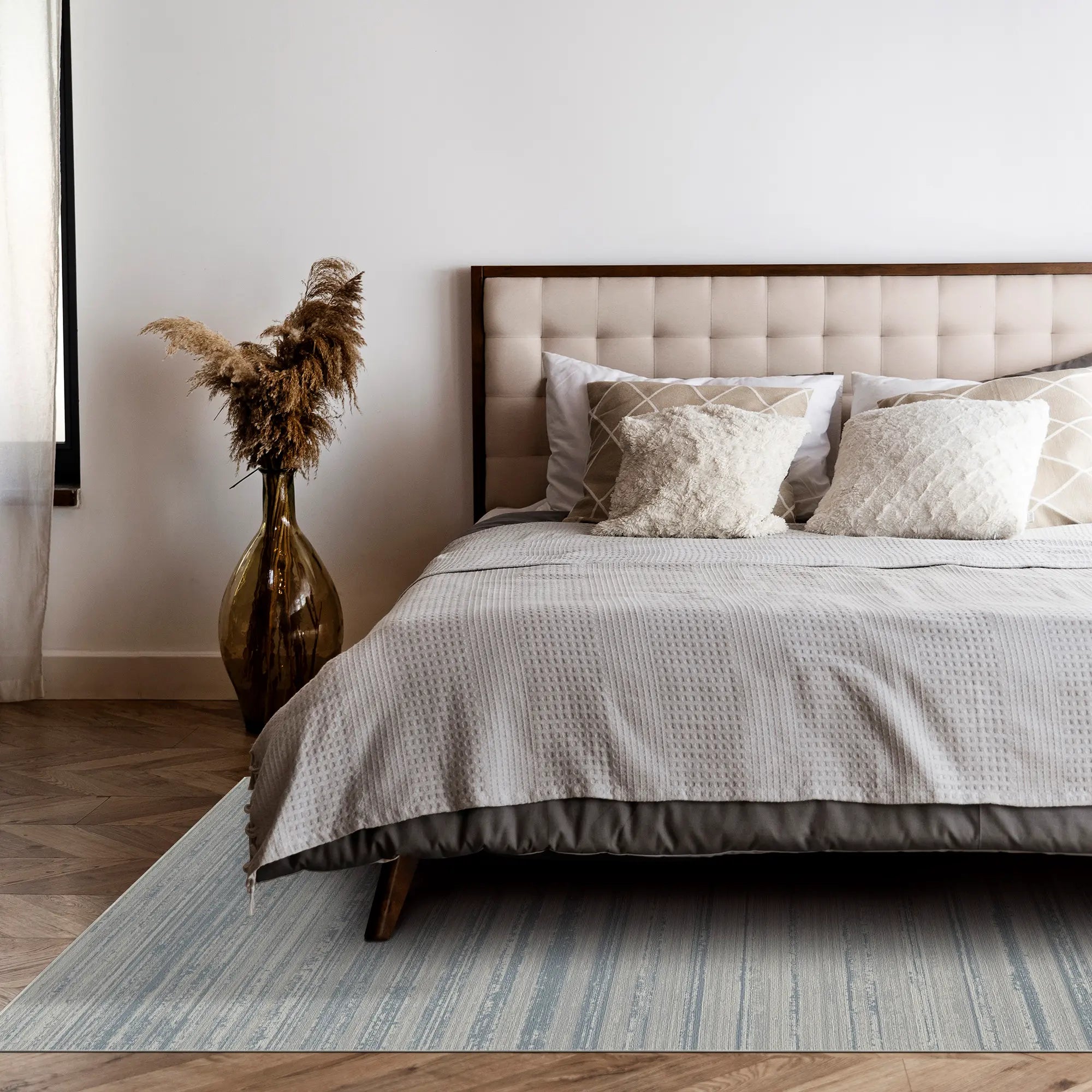 Blau-grau gestreifter Teppich unter dem Bett auf Holzboden im Schlafzimmer