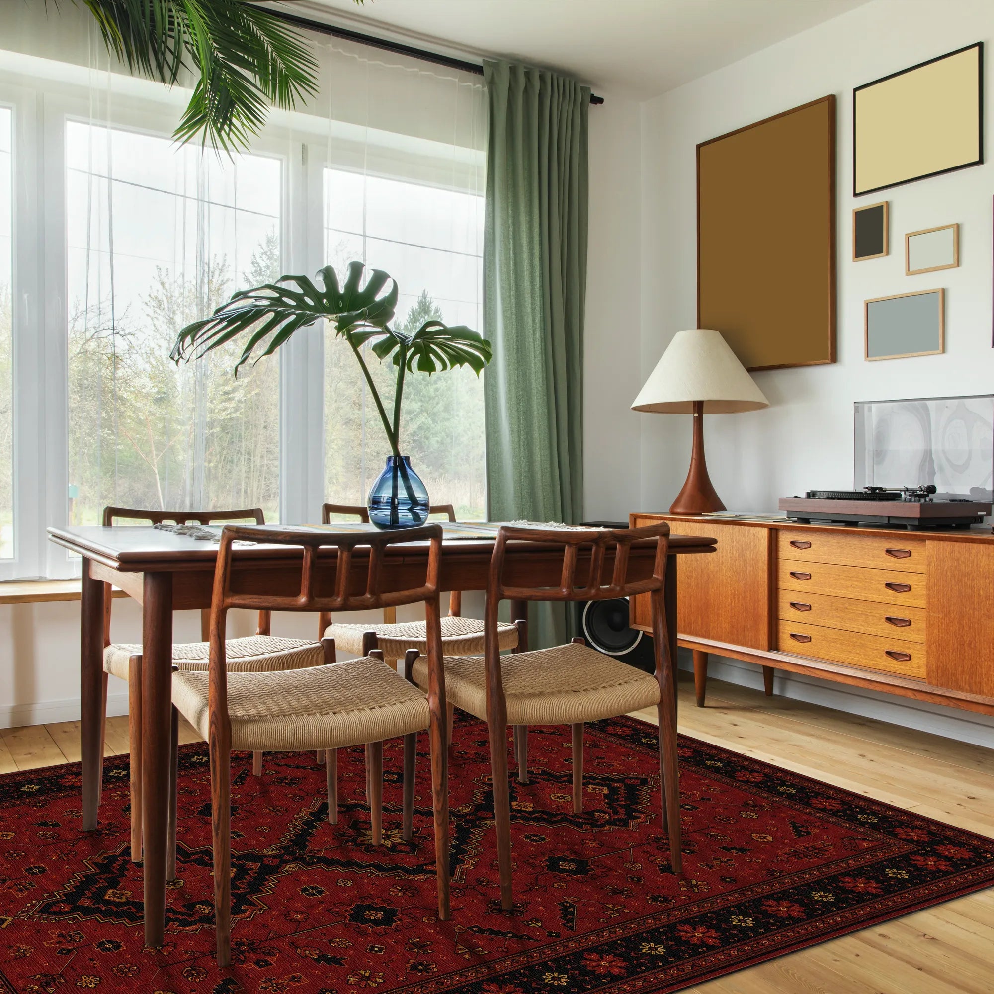 Ein Esszimmer im Mid-Century-Modern-Stil mit einem hölzernen Esstisch und vier Stühlen mit geflochtenen Rücken auf einem rot gemusterten Teppich. Der Raum hat einen hellen Holzboden, ein hölzernes Sideboard mit einer Lampe und einem Plattenspieler sowie ein großes Fenster mit grünen Vorhängen.